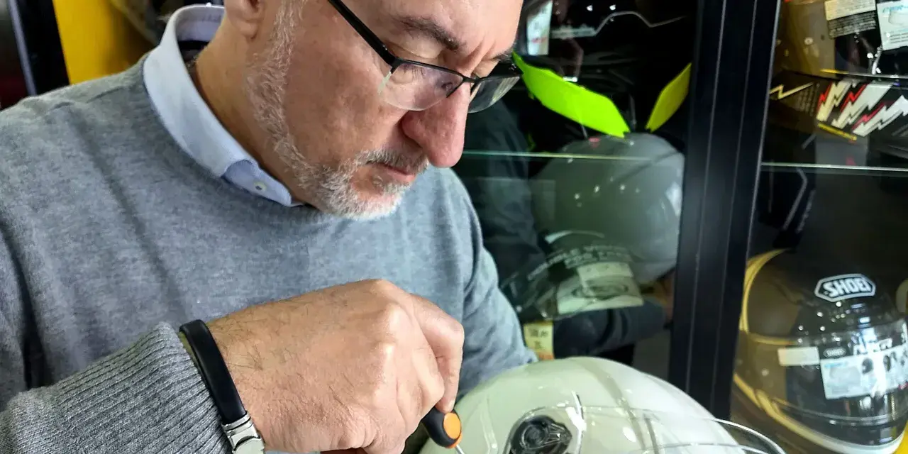 Uomo con cacciavite regola la visiera di un casco bianco, assicurandosi che il casco debba avere la visiera priva di graffi.
