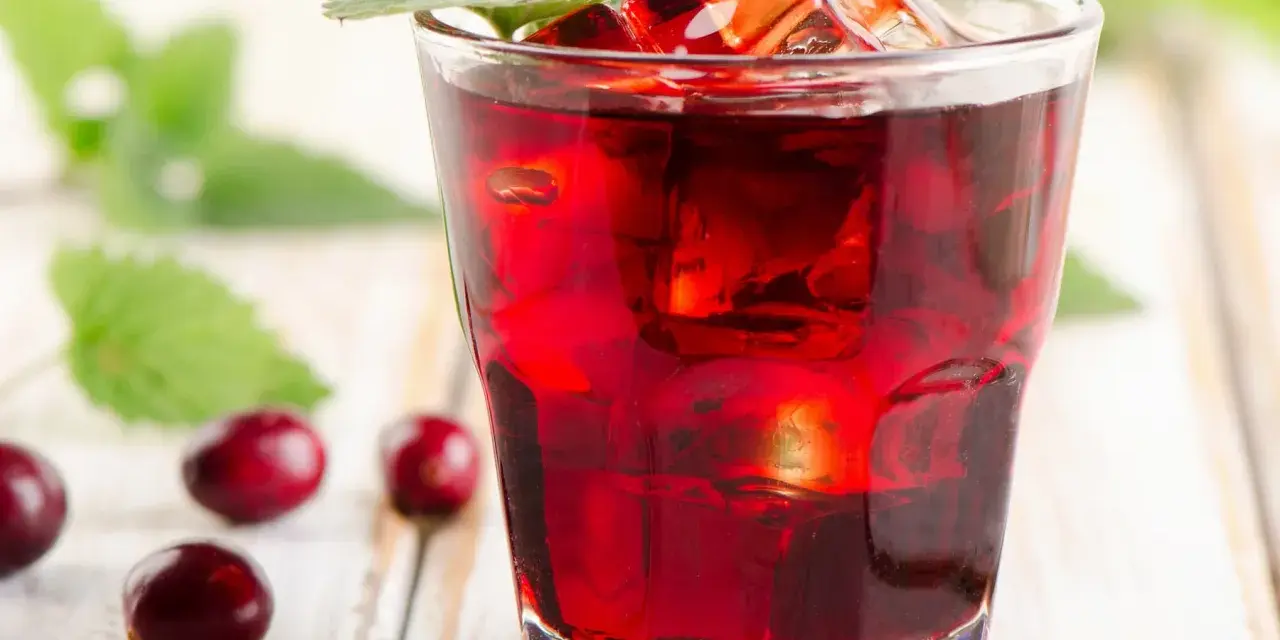 Orzeźwiający drink z żurawiną, lodem i listkiem mięty, otoczony kilkoma owocami żurawiny na drewnianym tle.