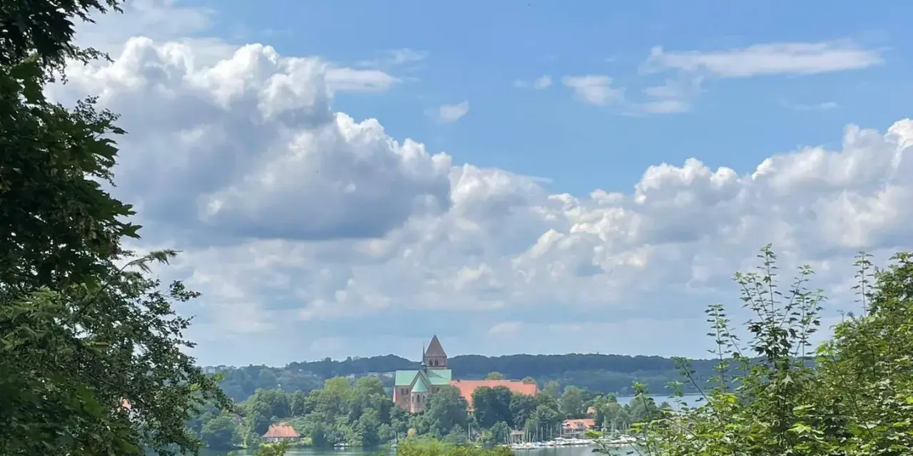 Blick auf die Ratzeburg Altstadt mit Domkirche, umgeben von grünen Bäumen und dem See unter einem dramatischen Wolkenhimmel.