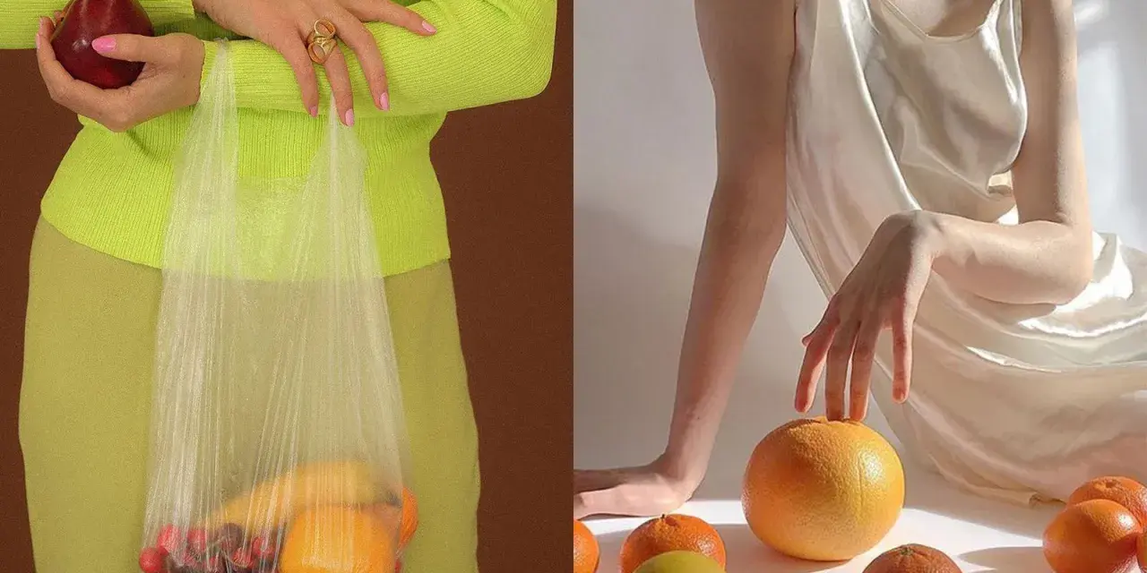 Mani che tengono una mela e una busta con ciliegie e arance. Altre arance e un limone sparsi su uno sfondo chiaro, evocando un'essenza di fruit extract.