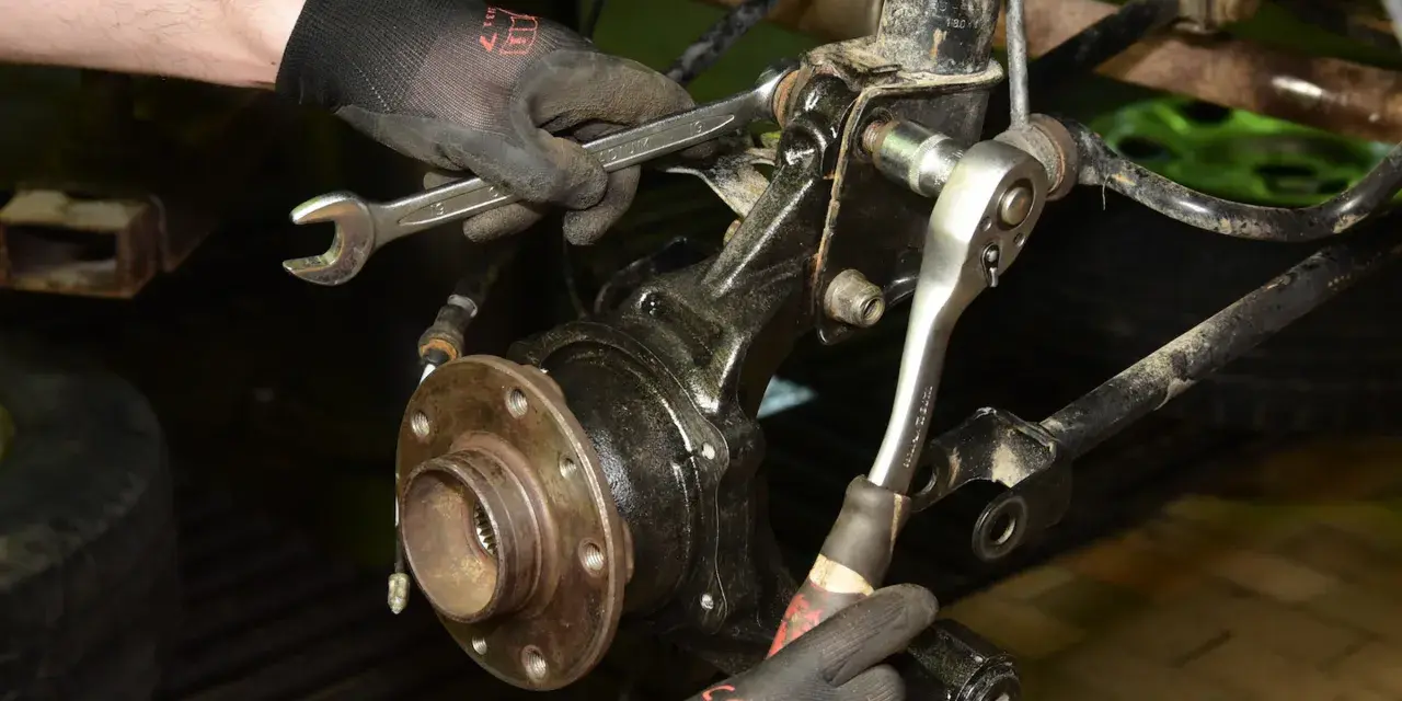 Mechanik dokręca śruby przy piaście, wymieniając łożysko w samochodzie.