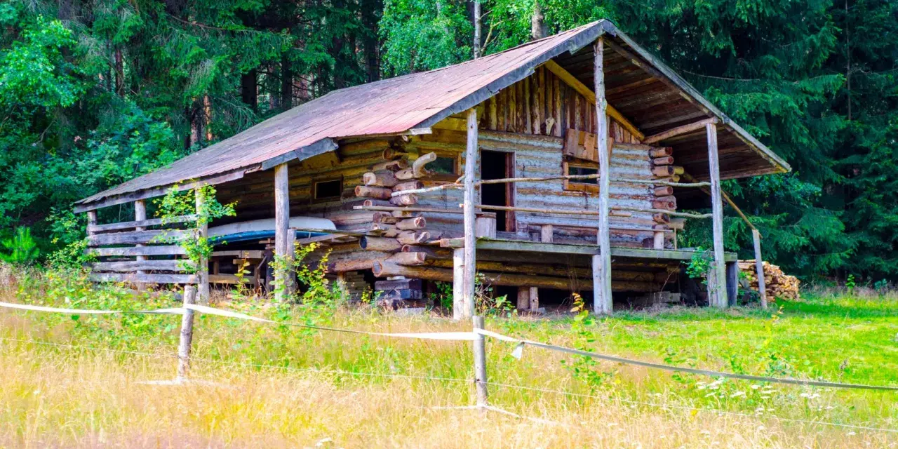 Drewniany bieszczady domek na odludziu, otoczony lasem i łąką. Wygląda jak miejsce na spokojny wypoczynek z dala od cywilizacji.