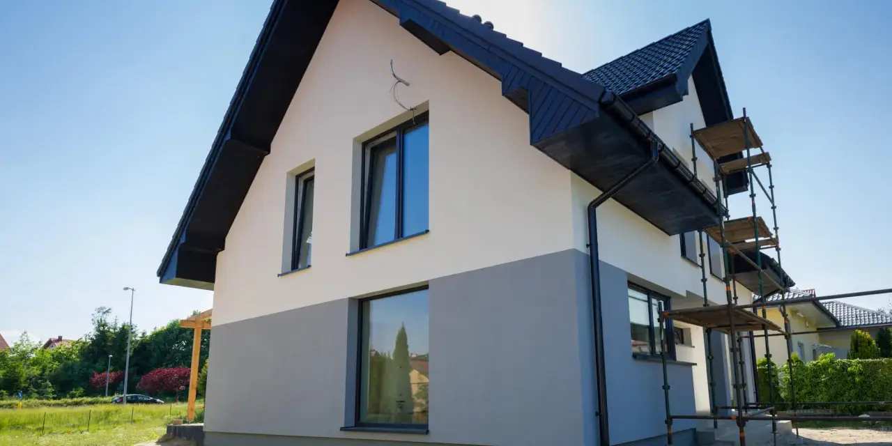 Nowy dom z dwukolorową elewacją, biało-szarą, to świetny pomysł na elewację domu. Widać rusztowania, co sugeruje trwające prace.