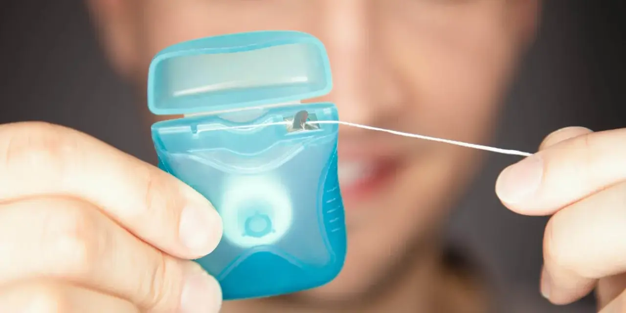 Mężczyzna trzyma niebieskie pudełko z nicią dentystyczną (floss).