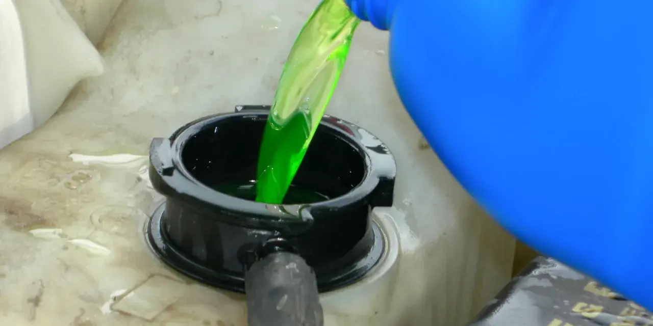 Green antifreeze is poured from a blue jug into a car's coolant reservoir. This raises the question: does antifreeze expire?