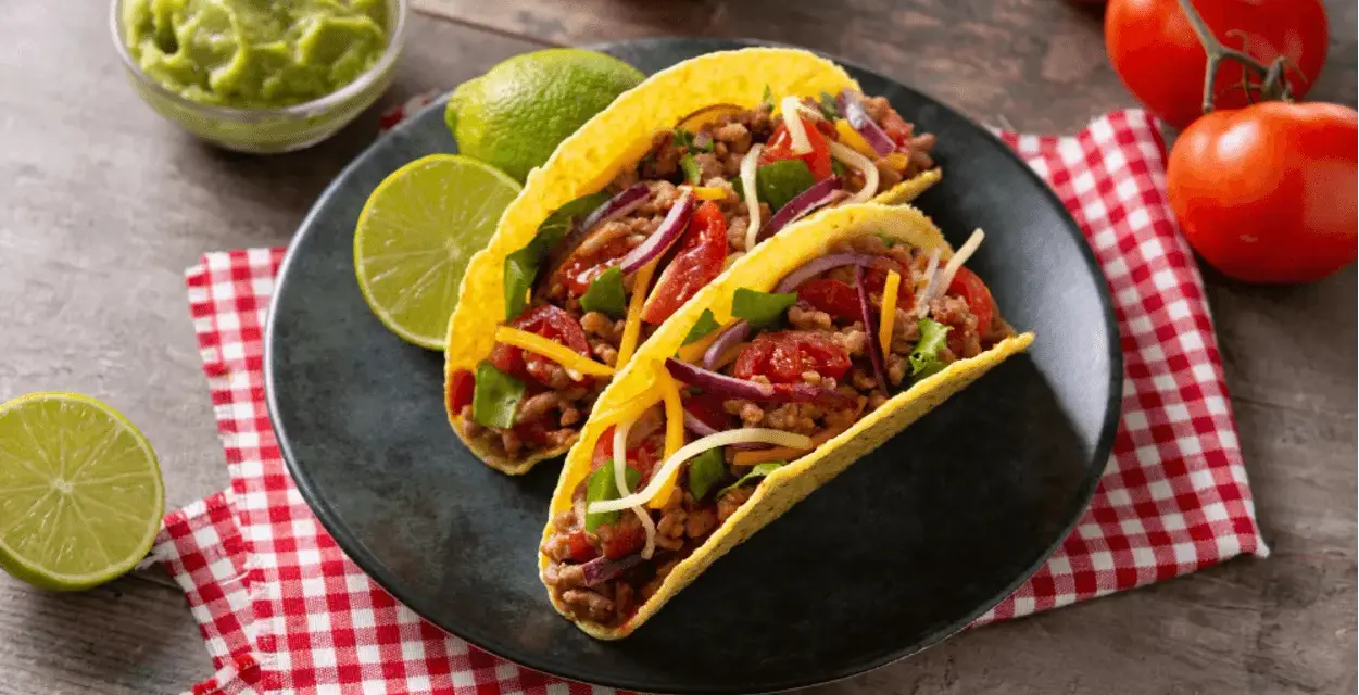 Dwa pyszne tacos z wołowiną, pomidorami, cebulą i serem, podane z limonką i guacamole.