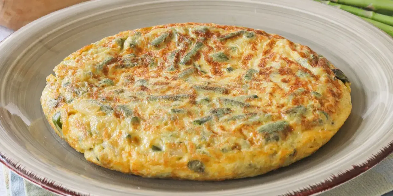 Tortilla de esparragos dorada y esponjosa, con trozos verdes de espárragos integrados en el huevo.