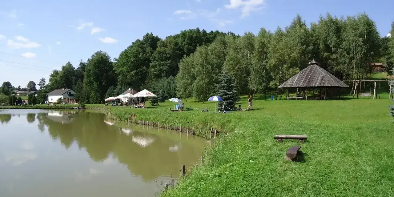 Malownicze dzikie łowiska Małopolska: spokojna woda, zielone wzgórza, drewniana altana i miejsca do wypoczynku.