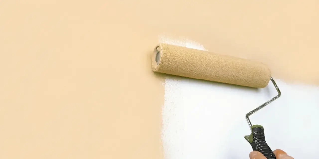 Rodillo pintando una pared de color melocotón con pintura blanca, buscando la mejor pintura antiruido para un hogar tranquilo.