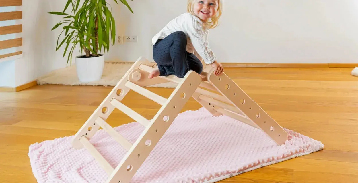 Ein fröhliches Kleinkind erkundet ein Pikler Dreieck. Ab wann Kinder damit spielen können, hängt von ihrer Entwicklung ab.