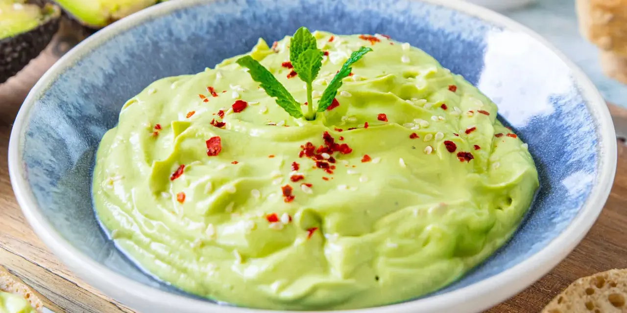 Cremige Avocado-Creme, garniert mit Minze, Sesam und Chiliflocken, serviert in einer blauen Schüssel. Perfekt als Dip oder Brotaufstrich.