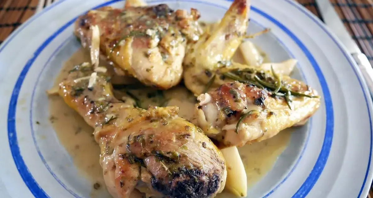 Delicioso pollo al ajillo servido en un plato azul y blanco, con trozos de pollo jugosos y dorados bañados en una salsa aromática con hierbas y ajo.
