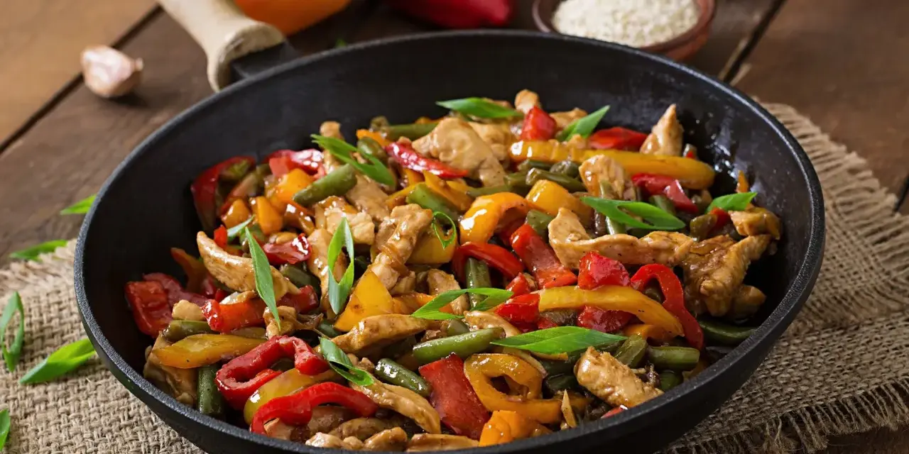 Straccetti di pollo con peperoni colorati e fagiolini, un piatto saporito e invitante servito in padella.