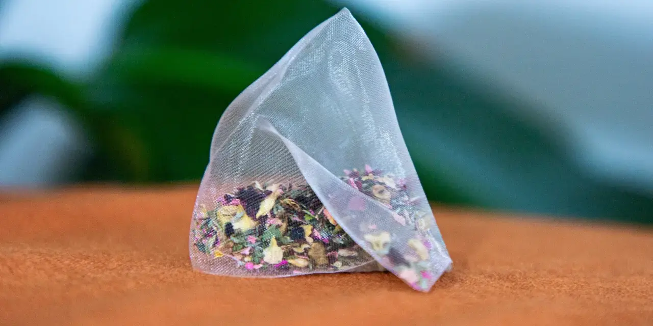 Un sachet de tisane pour anémie, rempli d'herbes et de pétales de fleurs colorés, repose sur un tissu orange.
