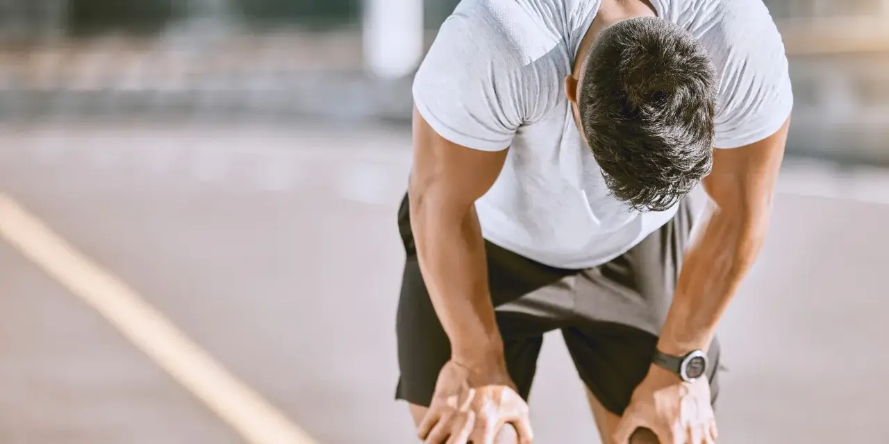 Atleta esausto con la testa china, mani sulle ginocchia, forse uno dei sintomi di overtraining.