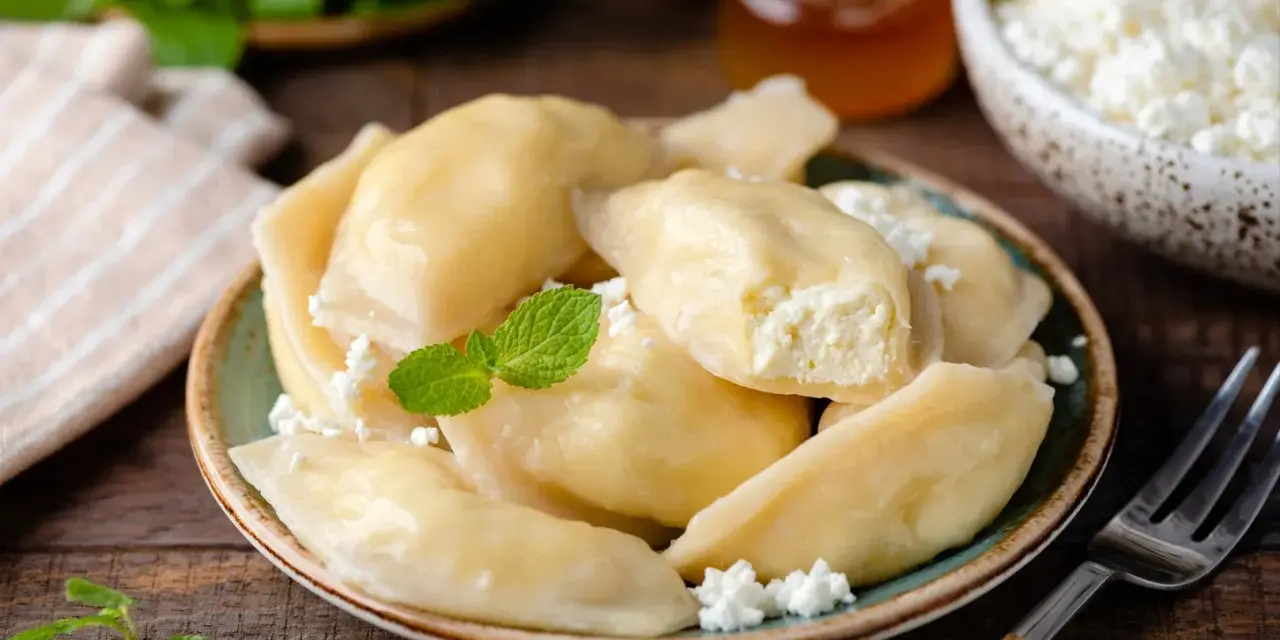 Pyszne pierogi z serem, jak u babci. Delikatne ciasto i kremowe nadzienie, posypane świeżym twarogiem i miętą.