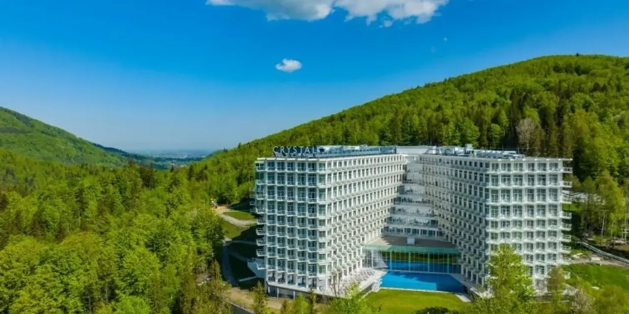 Nowoczesny Crystal Mountain Hotel Wisła otoczony zielonymi wzgórzami, z basenem i tarasami.