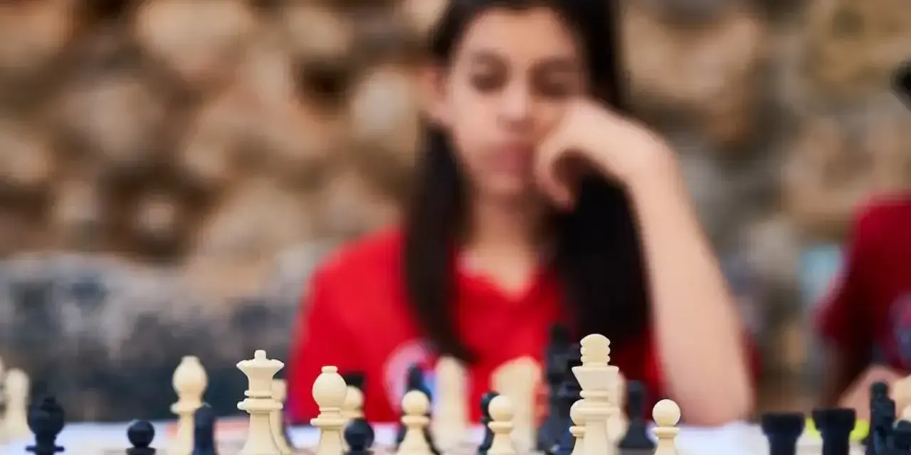 Niña pensativa frente a un tablero de ajedrez, inmersa en los juegos de decisiones.