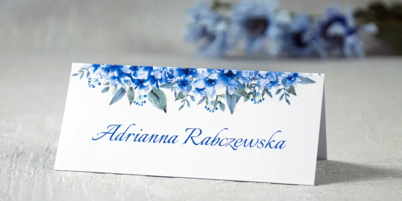 Eleganckie winietki dla usługodawców z motywem niebieskich kwiatów. Na białej kartce widnieje imię i nazwisko "Adrianna Rabczewska".