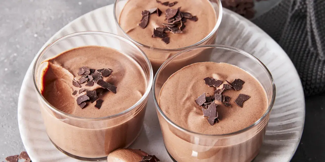 Drei Gläser mit luftiger Schokoladenmousse, garniert mit Schokostückchen. Ein Löffel zeigt die cremige Konsistenz dieses rezept mousse au chocolat ohne ei.