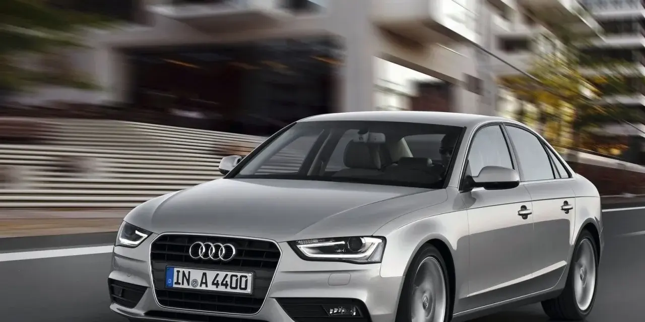 Srebrne Audi A4 B8 w ruchu miejskim, z rozmytym tłem budynków.