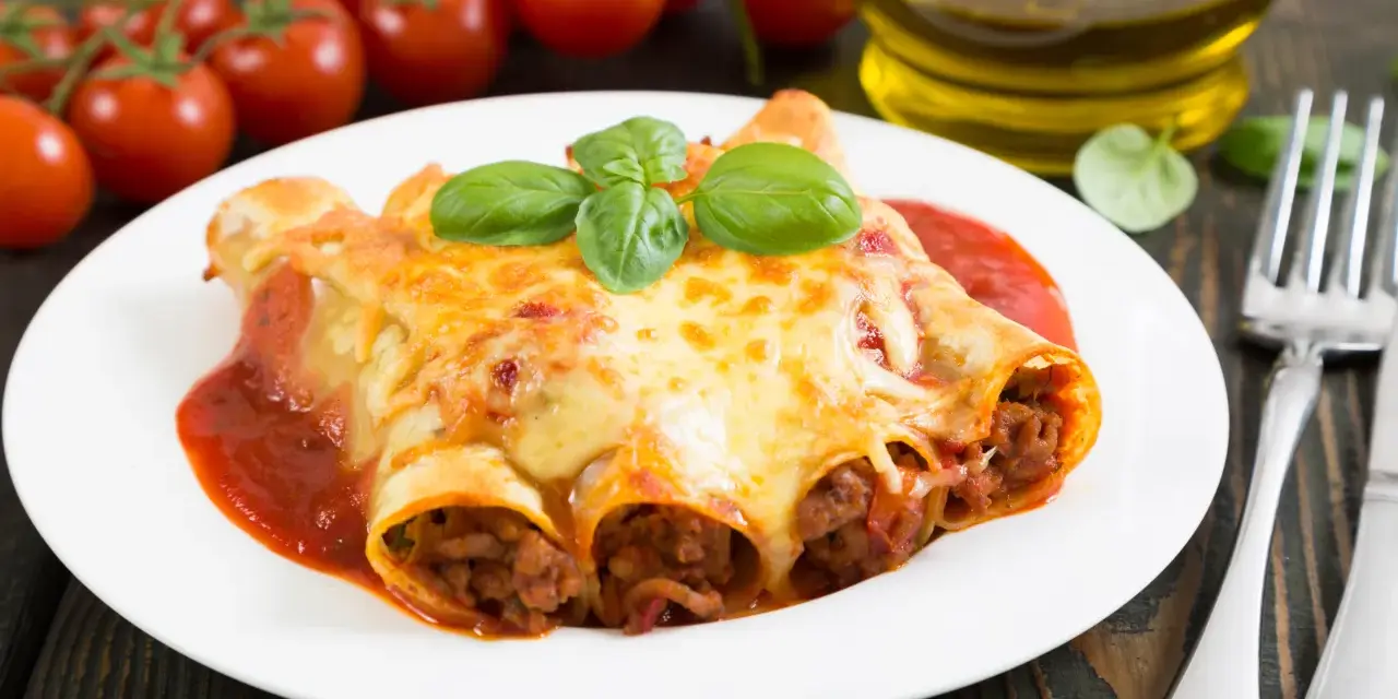 Cannelloni kontra naleśniki z mięsem: zapieczone w sosie pomidorowym i serze, ozdobione bazylią. Obok pomidorki i oliwa.