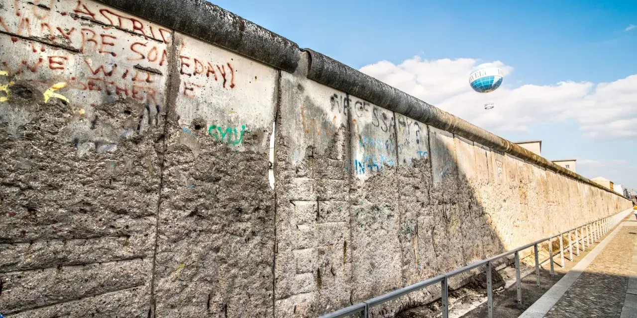 Beim Berlin Mauer besichtigen sieht man Graffiti und einen Heißluftballon.