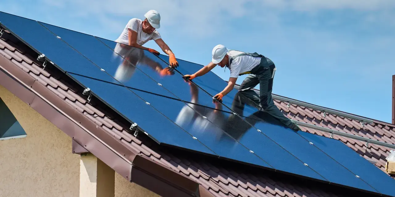 Dwóch monterów instaluje panele słoneczne na dachu. To przyszłość budownictwa, bo od września 2026 r. każdy nowy budynek musi posiadać magazyn energii.