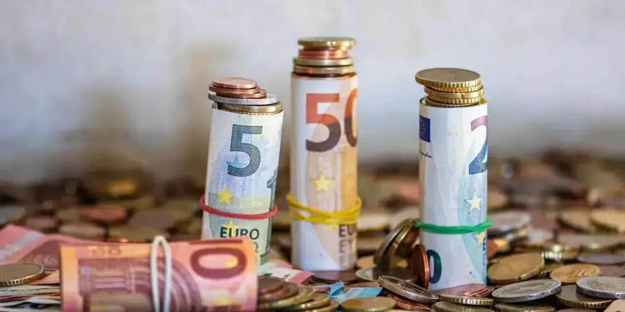 Zwijane banknoty euro i monety, symbolizujące kwotę darowizny wolną od podatku, tworzą stosy na tle innych monet.