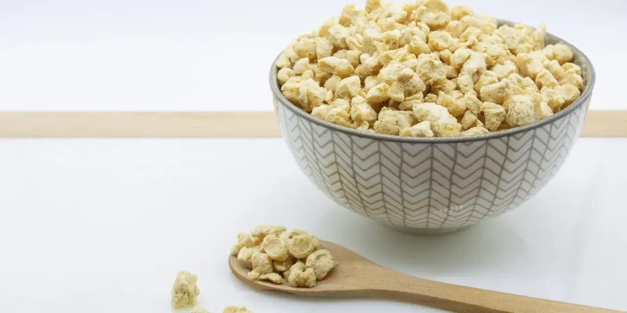 Un cuenco lleno de soja texturizada y una cuchara de madera con más de este ingrediente versátil.