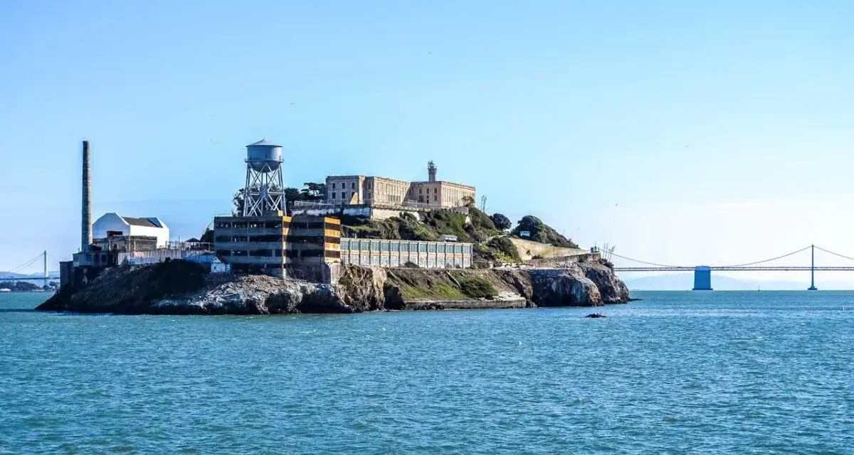 Słynne więzienie Alcatraz na skalistej wyspie, z charakterystyczną wieżą ciśnień i mostem w tle.