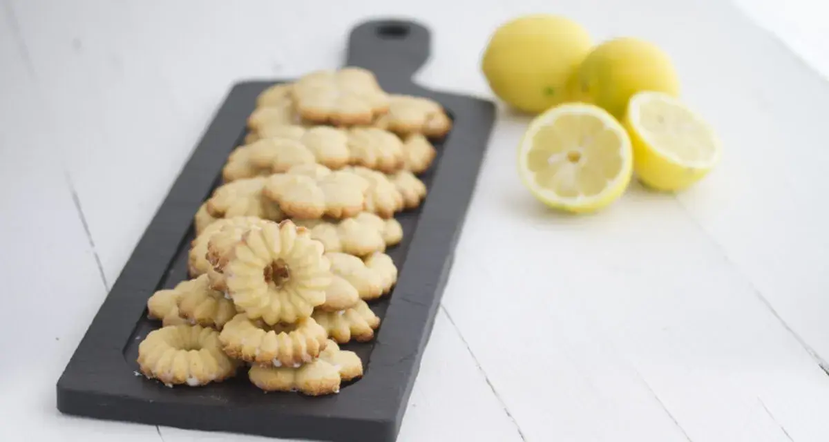 Deliciosas galletas de limón dispuestas en una tabla negra, con limones frescos al lado.
