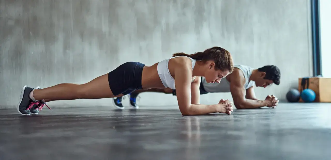 Un couple concentré fait la planche côte à côte dans une salle de sport.