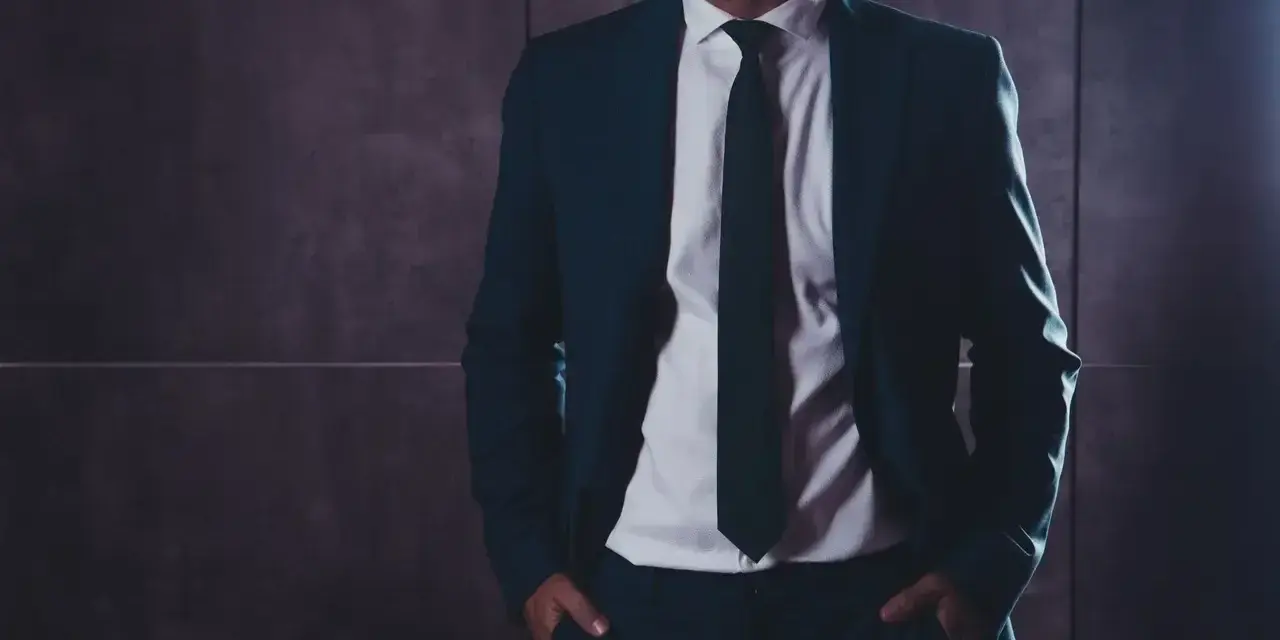 Elegancki mężczyzna w garniturze, z rękami w kieszeniach. Kim jest referent? To ktoś, kto reprezentuje, dba o szczegóły i buduje zaufanie.