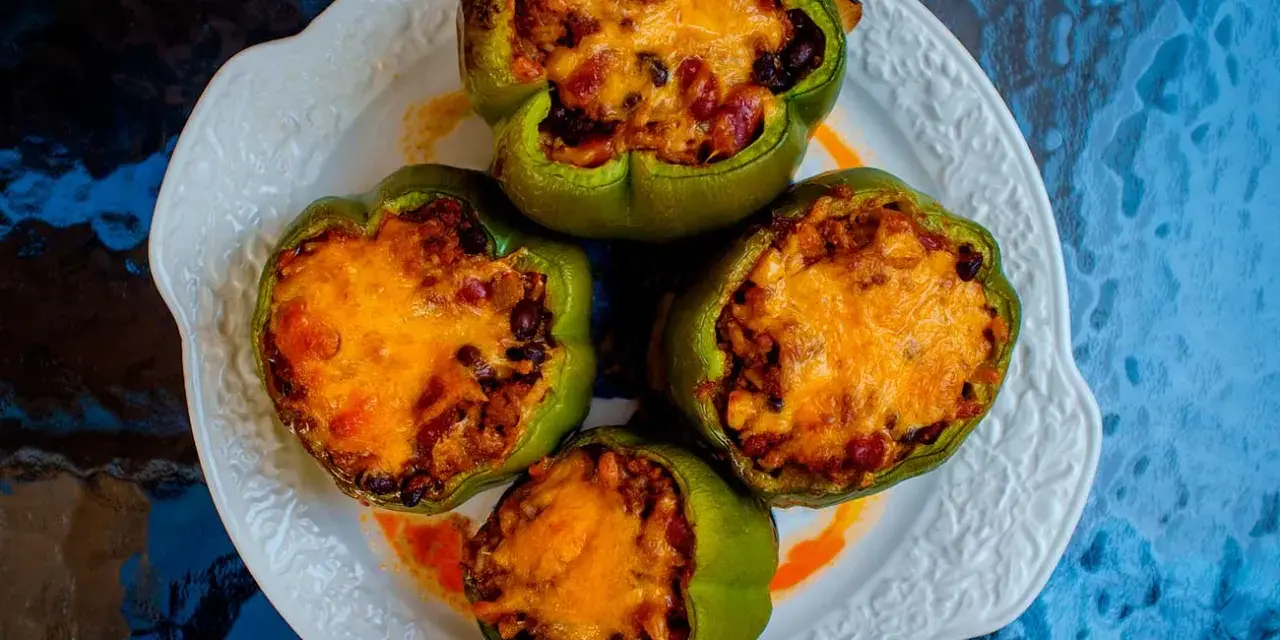 Cuatro pimientos verdes rellenos con carne, frijoles y arroz, cubiertos con queso derretido, servidos en un plato blanco.