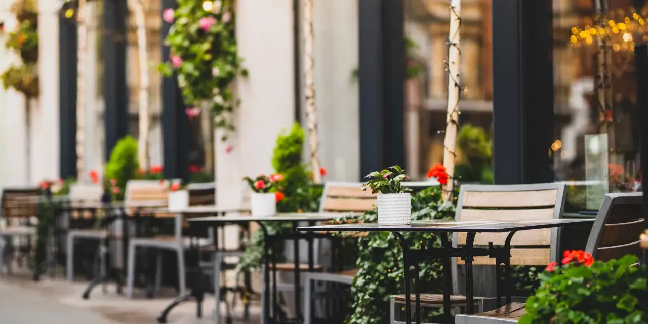 Mesas y sillas vacías en la terraza de un restaurante, adornadas con plantas y flores. Un lugar acogedor, listo para recibir clientes tras obtener las licencias de restaurantes.