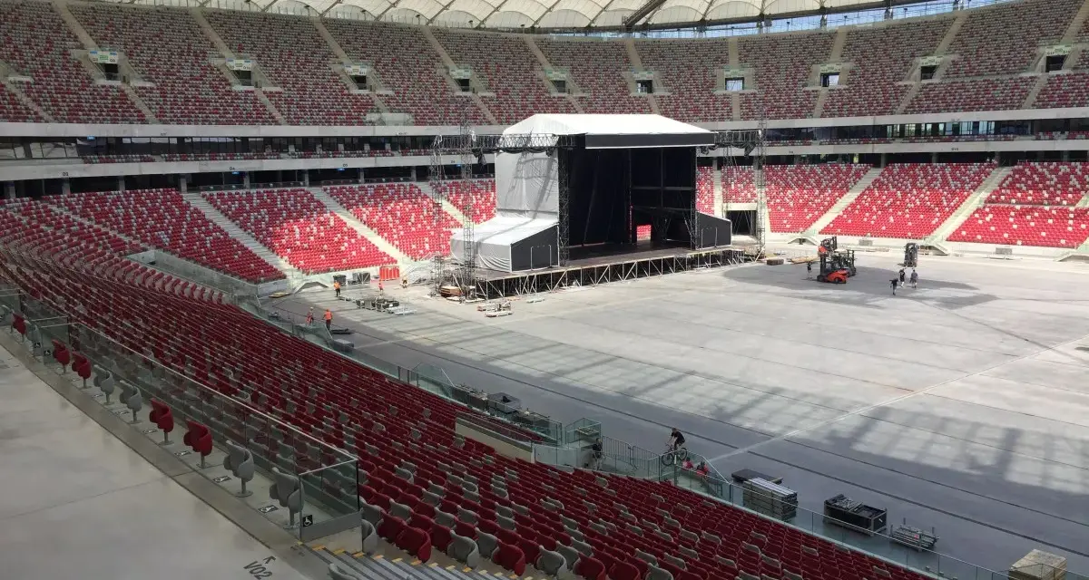 Przygotowania do koncertu Depeche Mode w Warszawie. Ogromny stadion z pustymi czerwonymi trybunami i sceną w budowie.