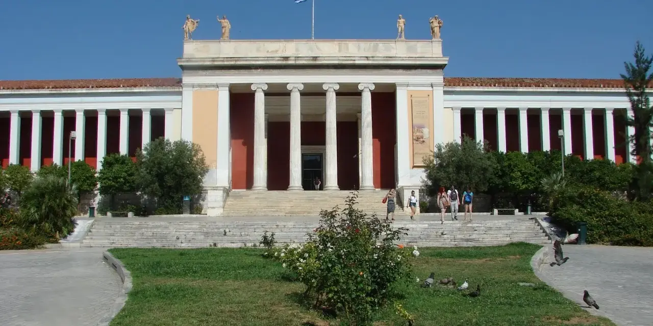 Narodowe Muzeum Archeologiczne w Atenach, z grecką flagą na dachu, zaprasza zwiedzających.
