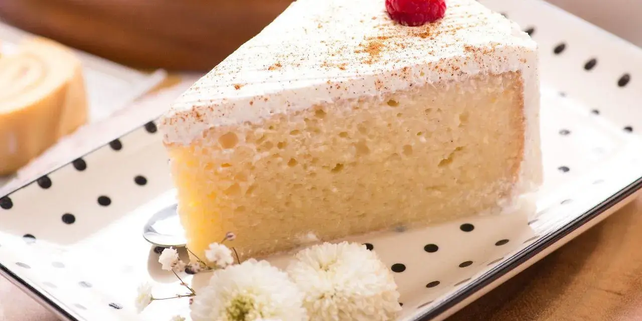 Pyszny kawałek ciasta Tres Leches, udekorowany maliną i cynamonem, czeka na spróbowanie. Idealny przepis na deser.