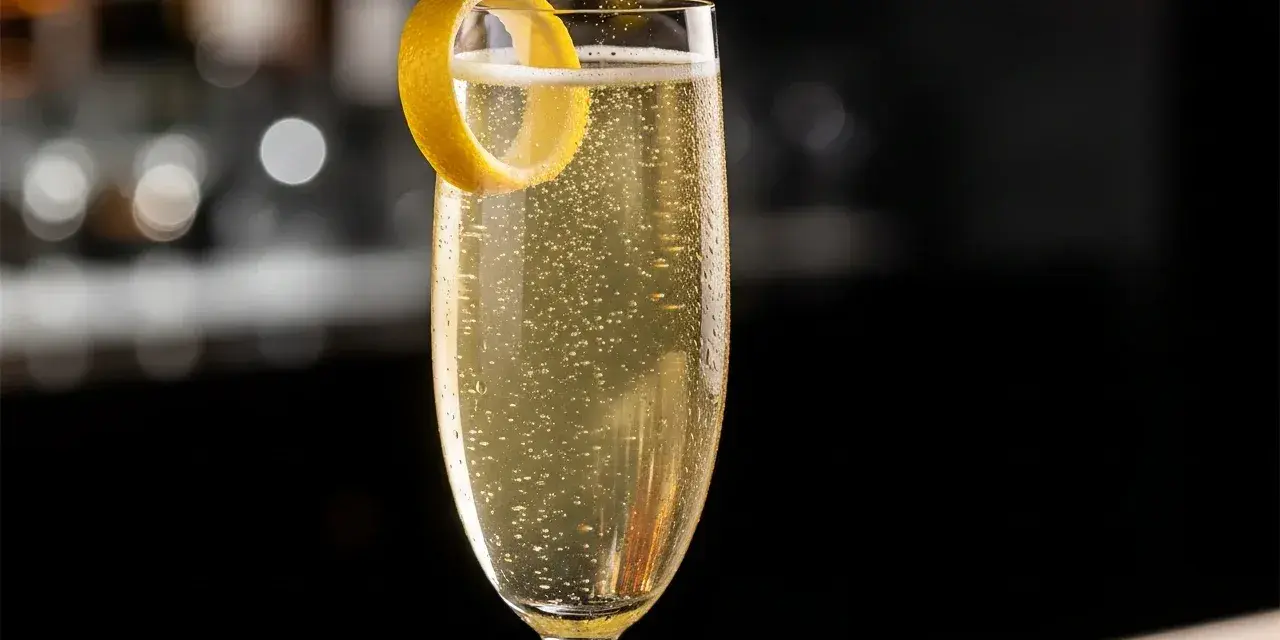 Ett glas French 75 med bubblor och citronskal. En klassisk drink med en intressant french 75 historia.