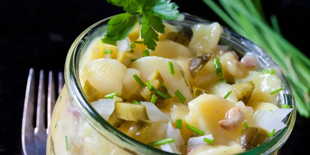 Ein köstlicher Kartoffelsalat ohne Mayo, mit Gurken und frischen Kräutern, serviert in einem Glas.
