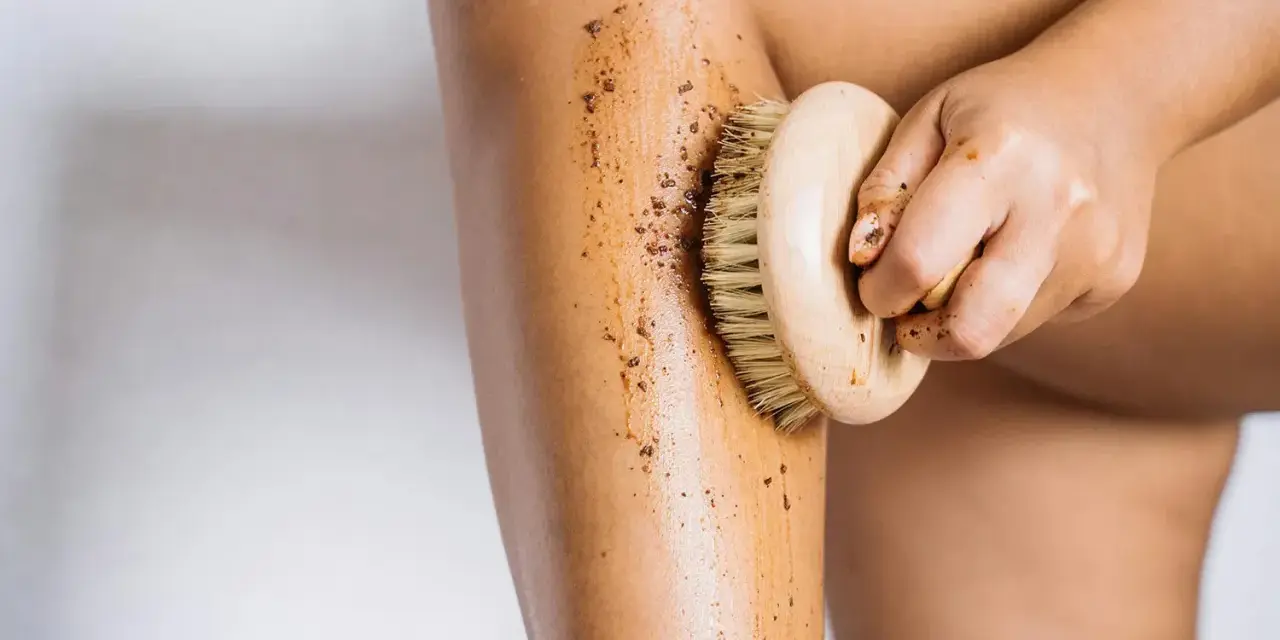 Exfoliación corporal con un cepillo de madera y un scrub para ayudar a como hidratar la piel desde dentro.