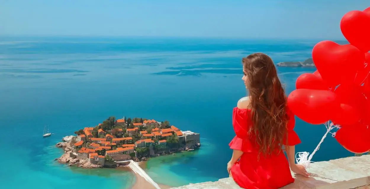 Marzenie o czarnogóra all inclusive samolotem? Kobieta w czerwonej sukni z sercami w ręku podziwia wyspę Sveti Stefan.