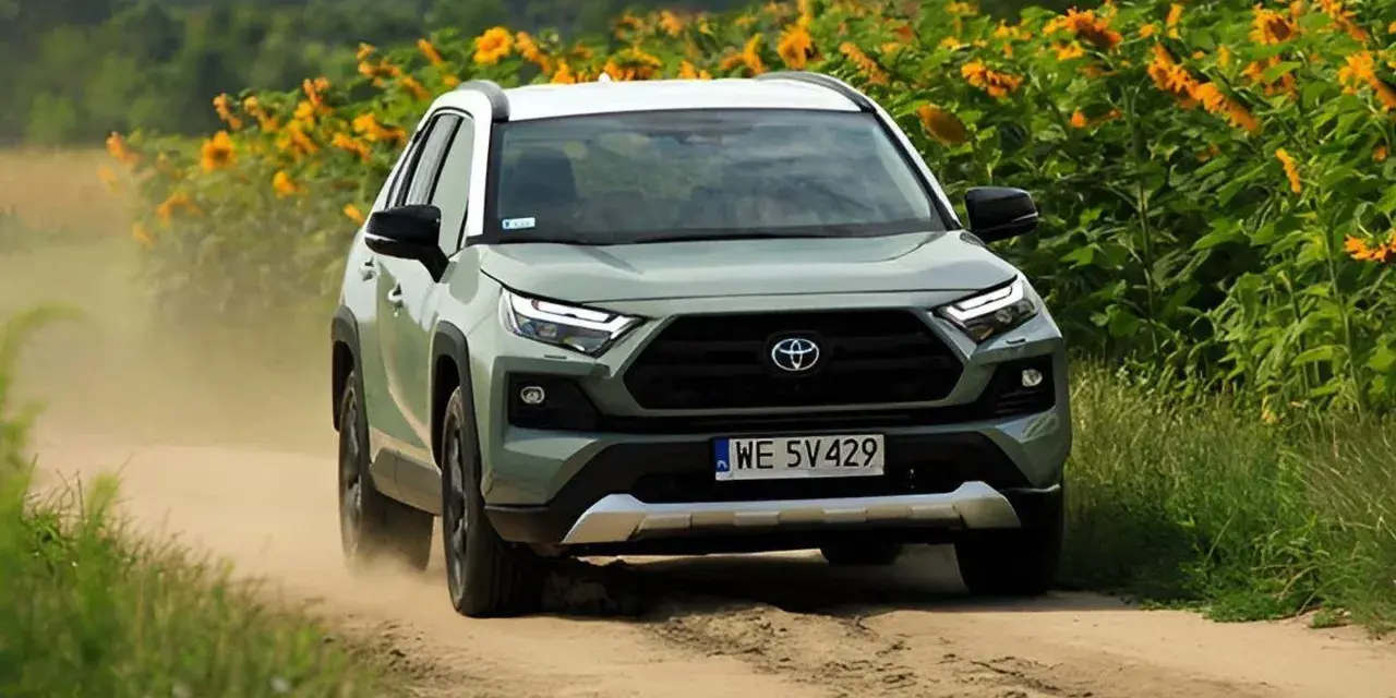 Zielona Toyota RAV4 jedzie po piaszczystej drodze, otoczona słonecznikami. To jeden z najmniej awaryjnych aut, gotowy na każdą przygodę.