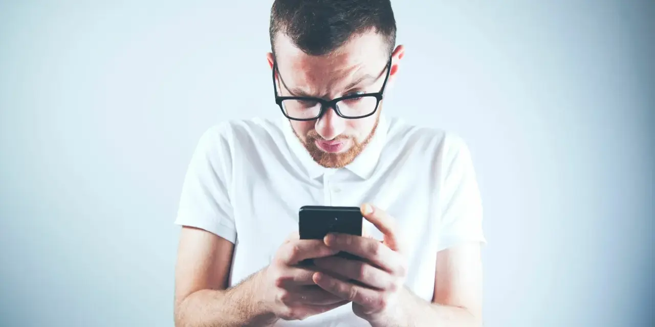 Zastanawiasz się, skąd firma windykacyjna ma Twój numer telefonu? Mężczyzna w okularach patrzy zdezorientowany na ekran smartfona.