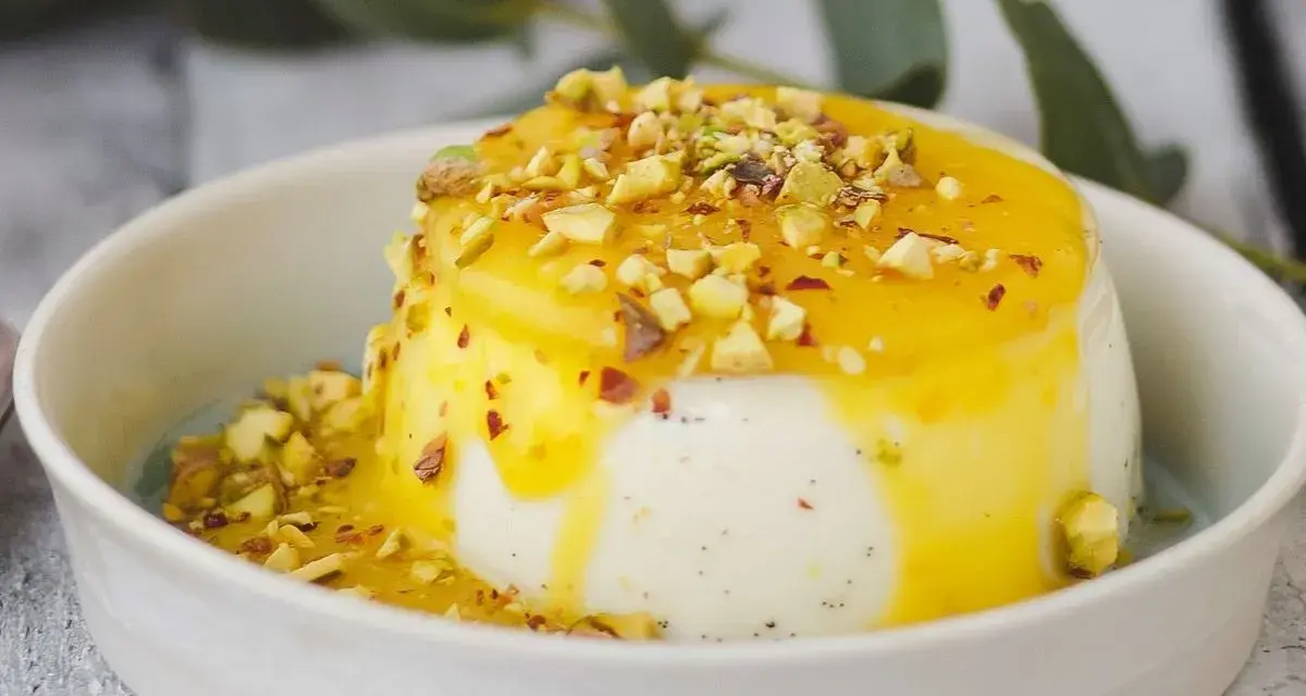 Budino fatto in casa cremoso, con salsa gialla e granella di pistacchi, servito in una ciotola bianca.