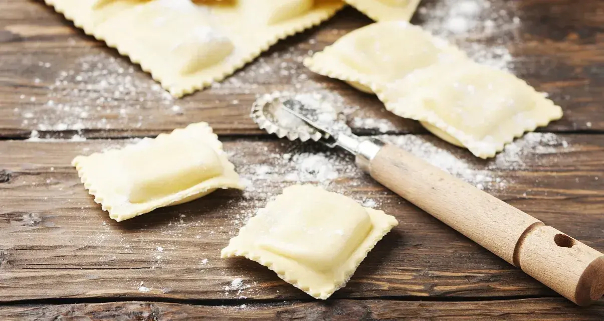 Świeże włoskie pierożki ravioli, różne rodzaje, gotowe do gotowania. Obok kółko do ciasta.