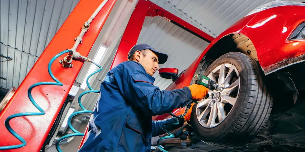 Mechaniker wechselt Reifen an rotem Auto. Informieren Sie sich, was kostet reifenwechsel, um Ihr Fahrzeug sicher zu halten.