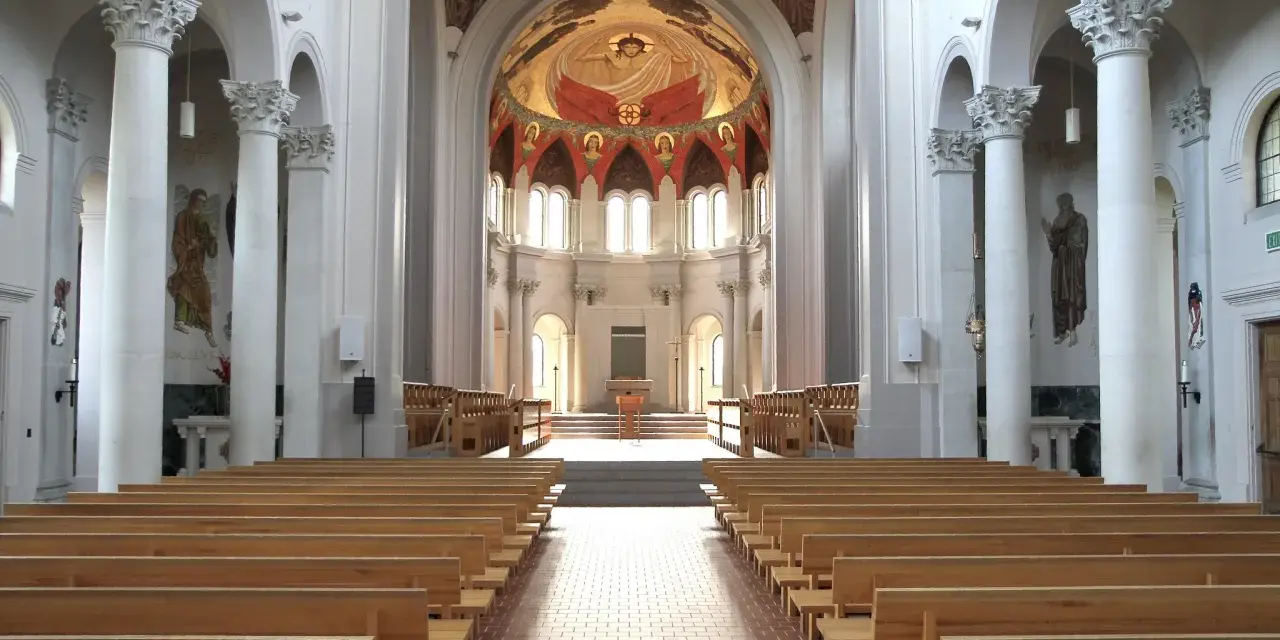 Interior of a grand abbey, with rows of wooden pews leading to an altar. The domed ceiling features a vibrant fresco. Check the abbey mass schedule for service times.