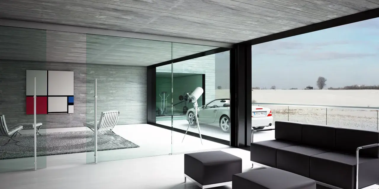 Interior moderno con sofá negro, sillones y una gran pared de cristal que da a un paisaje nevado y un coche descapotable.